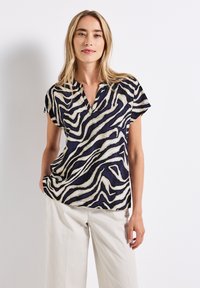 Short-sleeve blouse in navy and cream with an abstract zebra stripe pattern, featuring a v-neck and a loose-fitting design.