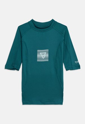 Rash guard à manches courtes couleur sarcelle avec col montant et logo abstrait blanc centré, coutures plates et logo sur la manche gauche.