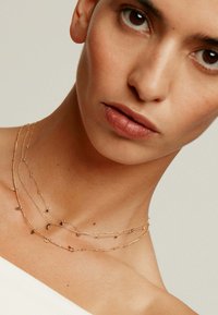 Collares de oro en capas con colgantes de diversas formas, diseño de cadena fina y acentos delicados sobre piel desnuda.