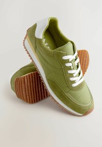 Grøn ruskind og stof sneaker med hvide accenter, tekstureret brun gummisål og hvide snørebånd. Har en afrundet tå og polstret krave.