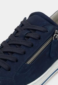 Ναυτικό μπλε σουέντ αθλητικό παπούτσι με επίπεδα ναυτικά κορδόνια, πλαϊνό φερμουάρ με ασημένια δόντια και λευκή λαστιχένια σόλα με μπλε λεπτομέρειες.