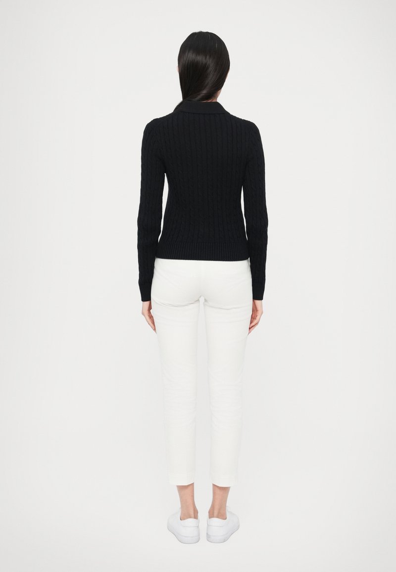 Mørkeblå strikket sweater med ribbet struktur, tætsiddende silhuet og lange ærmer, kombineret med hvide slim-fit bukser og hvide sneakers.