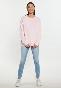 Roze sweatshirt met een ronde hals, lange mouwen en geribbelde boorden, gecombineerd met lichtblauwe jeans en witte sneakers. Eenvoudig en casual ontwerp.