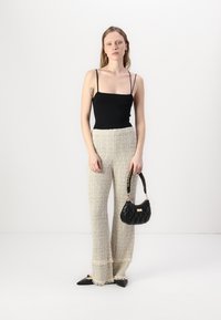 Svart tettsittende tanktopp, beige teksturerte bukser med frynset kant, svart vattert håndveske med kjedevogn, og spisse svarte leiligheter.