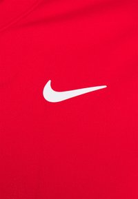 Punainen urheilu T-paita, joka on valmistettu tekstuurista kankaasta. Rinnassa on näkyvä valkoinen Nike-logoswosh.