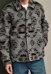 Fleecejacke in Grau mit braunen und schwarzen Mustern. Verfügt über einen Kragen, eine Knopfleiste vorne und eine einzelne Brusttasche. Strukturierter Stoff.