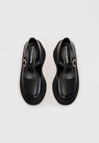 Μαύρα δερμάτινα παπούτσια Mary Jane με χοντρά πέλματα και ασημένιες αγκράφες, εμφανές το όνομα της μάρκας μέσα σε κάθε παπούτσι σε λευκό φόντο.