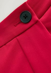 Primer plano de una prenda roja con un botón negro de cuatro orificios asegurado a través de un ojal cosido.
