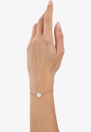 Pulsera de cadena de oro en una mano, con un charm circular que presenta patrones de estrellas grabados y una textura suave.
