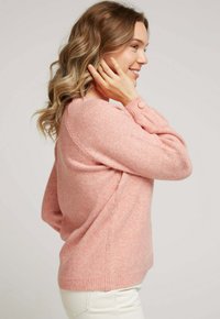 Pull en tricot rose avec une texture douce, doté d'un col rond et d'un détail de bouton sur la manche. Le design est de coupe décontractée.