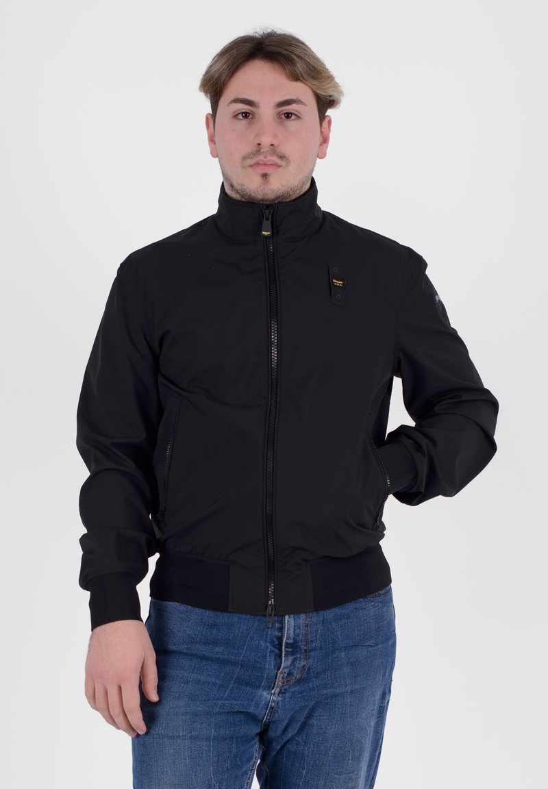 Giacca bomber nera con colletto alto, chiusura con zip e polsini a coste. Presenta una piccola patch con logo sul petto e tasche laterali.