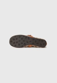 Brown woven sandal with a textured upper and a smooth rubber sole featuring floral patterns. Adjustable strap for fit.