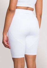 Białe prążkowane krótkie spodenki sportowe z wysokim paskiem, o dopasowanym kroju i tonalnych przeszyciach. Tekstura wydaje się miękka i elastyczna.
