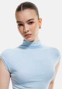 Top azzurro chiaro a collo alto con maniche a cappuccio. Il tessuto ha una texture liscia e il design presenta una silhouette aderente.