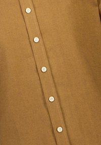 Bruine blouse met knopen, gemaakt van een gestructureerde stof, voorzien van zes crème knopen en een verticale sluiting, met een gladde, getailleerde afwerking.