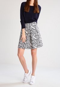 Black and white patterned skirt with a pleated design, paired with a black long-sleeve top and white sneakers.