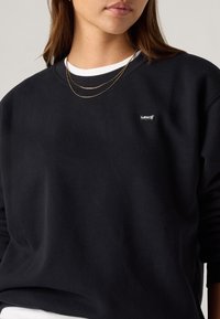 Μαύρο φούτερ από μαλακό ύφασμα, με λευκή στρογγυλή λαιμόκοψη και μικρό λογότυπο Levi's στο στήθος. Περιλαμβάνει στρωματωτά χρυσά κολιέ.