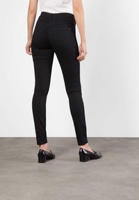 Sorte skinny jeans med høy midje, to baklommer og en glatt teksturert overflate, kombinert med svarte hælsko.