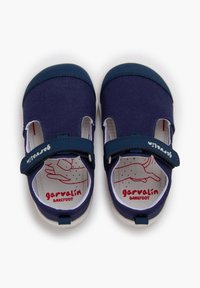 Zapatillas de lona azul marino con suelas de goma blanca, una correa de velcro y laterales remarcados. Presentan un diseño de plantilla en rojo y blanco con la marca "garvalin".