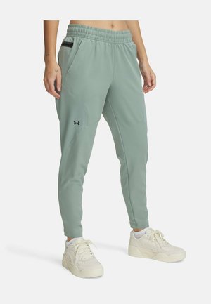 Light green athletic joggers with an elastic waistband, side pockets, subtle seams, and a logo on the left thigh. Paired with white sneakers.