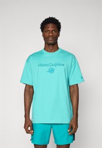 Camiseta de algodón turquesa con el texto y el logotipo de "Miami Dolphins" en azul más oscuro. Mangas cortas, cuello redondo, ajuste relajado.