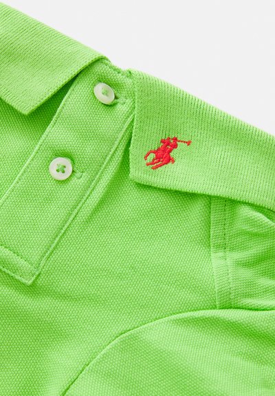 Žalias medvilnės polo marškinėliai su klasikinėmis apykaklėmis, dviem mygtukais ir mažai raudonai siuvinėta logotipu ant apykaklės. Textūruota medžiaga.