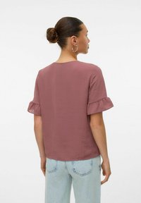 Top a maniche corte in tessuto rosa polveroso con una morbida texture, caratterizzato da maniche a volant e una vestibilità comoda, abbinato a jeans azzurri chiari.