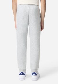 Grå joggebukser med smal passform, elastisk midjebånd, sidelommer og ribbestrikkede mansjetter, kombinert med hvite joggesko med blå detaljer.