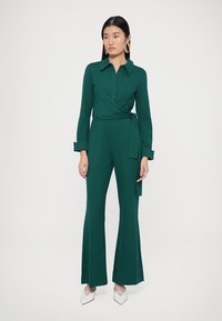 Groene jumpsuit in wikkelstijl met kraag, lange mouwen en wijde, uitlopende pijpen. Soepele stof met een ceintuur om zelf te knopen en knoopdetails.