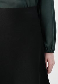 Zwarte gebreide rok met een textuurafwerking, voorzien van een brede tailleband en een soepel groene blouse. De zoom is iets uitlopend.