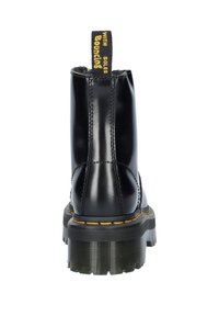 Bottine en cuir noir avec une semelle épaisse texturée, des coutures jaunes et une languette noire étiquetée "AVEC DES SEMELLES QUI REBONDISENT."