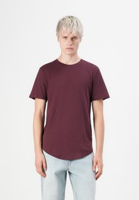 Burgunderfarbenes T-Shirt mit kurzen Ärmeln und Rundhalsausschnitt, weicher Textur und abgerundetem Saum, kombiniert mit hellblauen Jeans.