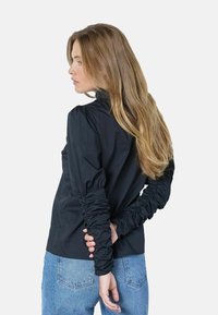 Zwarte top met hoge hals en gerimpelde mouwen, gecombineerd met lichtblauwe denim jeans. Gladde stoftextuur en aansluitend ontwerp.