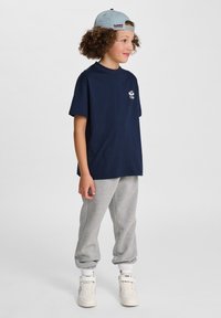 Marinblå bomullströja med korta ärmar, kombinerad med ljusgrå sweatpants och vita sneakers. En ljusblå keps kompletterar den avslappnade looken.