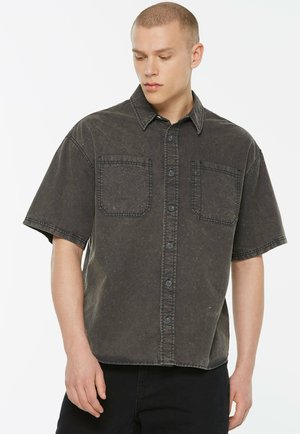 Kurzärmliges, dunkelgraues Hemd mit Knöpfen und zwei Brusttaschen, aus Baumwolle gefertigt, mit einer verblichenen Textur und sichtbaren Nähten.