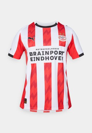 Sarkans un balts vertikāli svītrots futbols krekliņš ar zigzaga rakstiem, ar Puma logo, PSV Eindhoven emblēmu un melnu apdari ap kaklu.