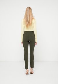 Ελιά πράσινο στενό παντελόνι με ομαλή υφή και τσέπες κανονικού μεγέθους, συνδυασμένο με εφαρμοστή μακρυμάνικη κίτρινη μπλούζα, εμφανιζόμενο από πίσω.