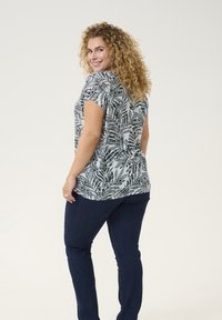 Top a maniche corte con un motivo di foglie blu, realizzato in tessuto morbido. Abbinato a jeans blu scuro, che mettono in mostra un fit rilassato.