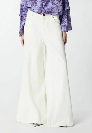 Pantaloni bianchi a gamba larga indossati con una camicia a maniche lunghe viola fantasia, con bottoni frontali e scarpe appuntite con stampa a serpente.