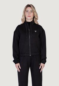 Juodas zip-up gobtuvas su didelėmis priekinėmis kišenėmis, lengvas audinys ir reguliuojami raišteliai. Logotipo detalė krūtinėje. Savybė: laisvas siluetas.