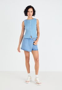 Lichtblauw, geribbeld mouwloos topje met knopen aan de voorkant en een kleine opening aan de zoom, gecombineerd met een gelaagde denim minirok. Witte sneakers met accenten.