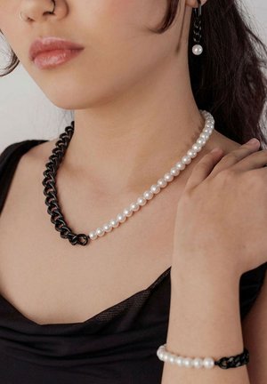 Frau mit schwarzer und weißer Perlenkette, passendem Armband und einzelnen Perlen-Ohrring mit schwarzen Kettenglied-Akzenten.