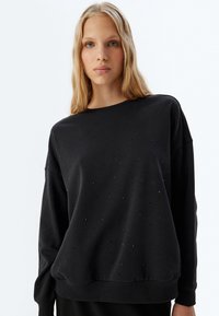 Felpa nera con scollatura rotonda e spalle cadenti, caratterizzata da piccoli dettagli decorativi e orli e polsini a coste.