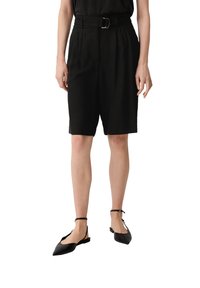 Shorts noirs ajustés avec une taille ceinturée, des plis à l'avant et des poches latérales. Assortis avec des ballerines noires à bout pointu et un haut noir.
