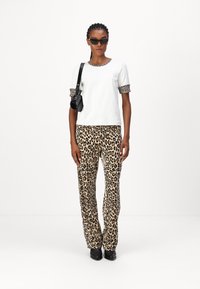 White short-sleeve top with leopard print cuffs, paired with straight-leg leopard print pants. Black sunglasses and small black bag included.