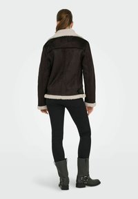 Bruine schapenvacht gevoerde jas met een zwarte buitenkant, voorzien van een ceintuur in de taille en brede manchetten. Gekozen boven een strakke zwarte broek en grijze laarzen.