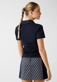Granatowa koszulka polo z krótkimi rękawami i kołnierzykiem, zestawiona z wzorzystą spódnicą o geometrycznym wzorze w kolorach granatowym i białym.