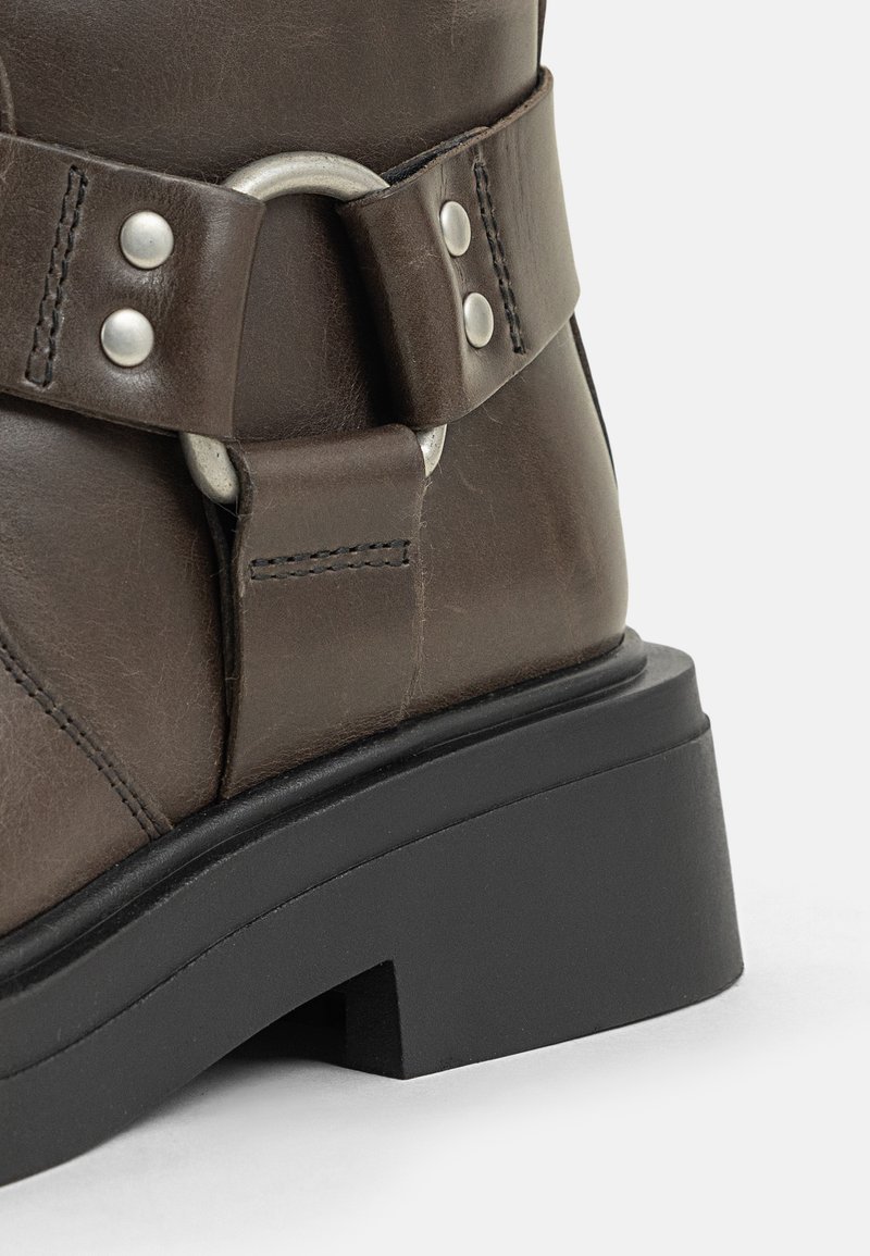 Braune Leder-Stiefelette mit einem Schnallenriemen, silbernen Hardware-Elementen, strukturiertem Obermaterial und einer klobigen, schwarzen Plateausohle.