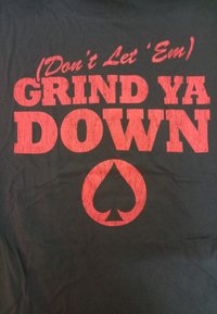 Svart t-shirt med fet röd text: "(Låt dem inte) SLITA NER DIG" med en spadeikon längst ner. Texten har en sliten struktur.