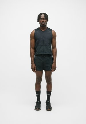 Svart atletisk väst med dragkedja och två framfickor, ihop med svarta shorts. Bärs med svarta höga strumpor och svarta löparskor, minimalistisk design.